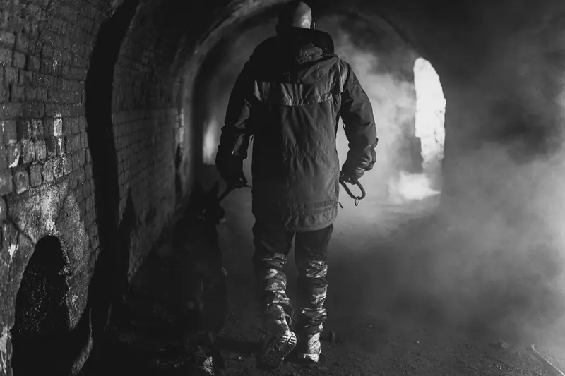 Handler walking with a dog through a smoky brick passageway.